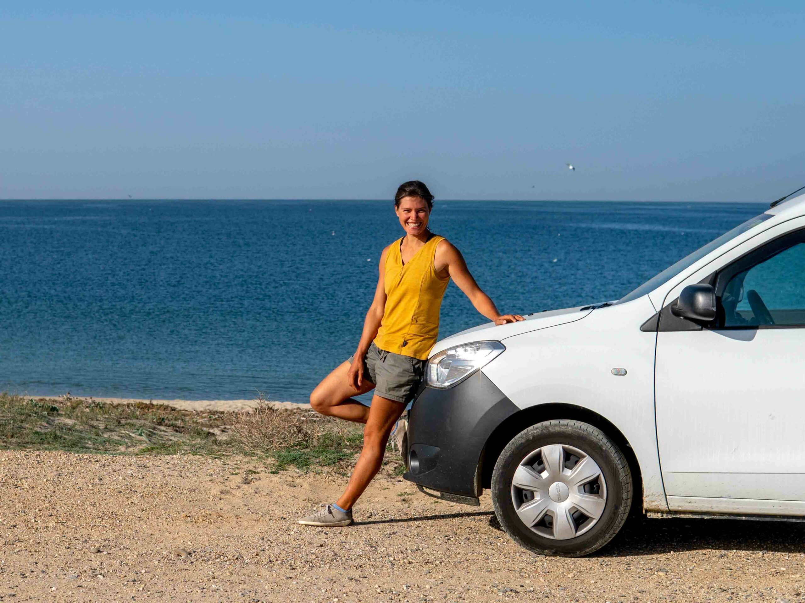 Die freie Journalistin Jule Rabe lehnt an einem Auto, im Hintergrund ist das Meer zu sehen.